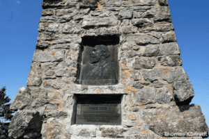 Gedenkstein für Bergsteiger an einem Felsen, mit Inschrift und Relief.