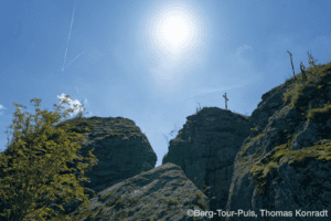 Bergtour im Sonnenschein mit Gipfeln und Kreuz auf den Felsen.