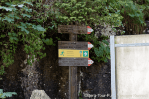 Wanderweg-Schild mit Richtungen in einer grünen Naturkulisse.
