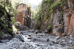 Bergtour in einer felsigen Schlucht mit Wasserlauf und grünen Bäumen.