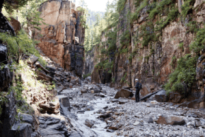 Bergtour in einer engen Schlucht mit steilen Felswänden und Flusslauf, Wanderer erkunden die Natur.