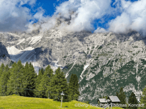 Alpenberg mit Gipfel, Wolken und grüner Wiese.