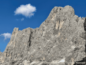 Felswand mit schroffen Klippen, blauer Himmel und Wolken im Hintergrund.