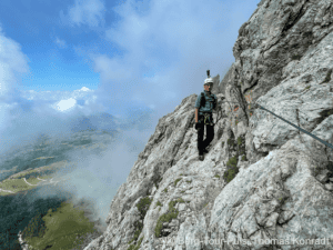 Bergsteiger auf Klettersteig in den Alpen mit Blick auf die Berge und Wolken.