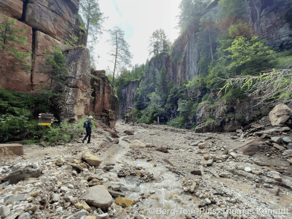 Bergtour in einer felsigen Schlucht mit Wasserlauf und umgeben von hohen Felswänden.