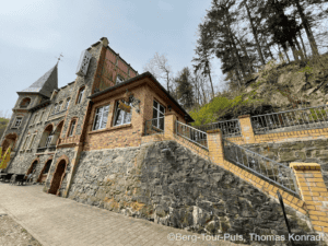 Historisches Gebäude mit steiler Treppe und Wald im Hintergrund.