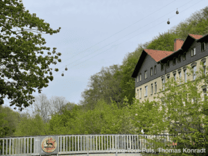 Blick auf historische Gebäude und Seilbahn in grüner Berglandschaft.