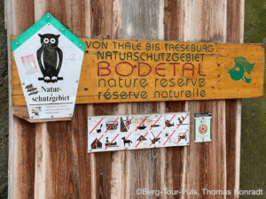 Naturschutzgebiet Bodetal mit Warnhinweisen und Tierschutzsymbol an Holzschild.