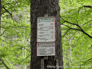 Hiking trail sign in a lush green forest with multiple route directions and distances.