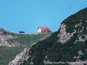 Berggasthof auf einer grünen Bergwiese mit Blick auf die Küste.