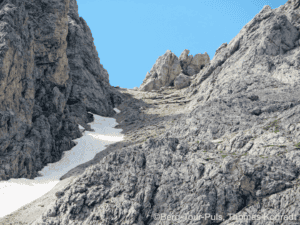 Alpenbergwand mit Schneefeldern, Bergsteiger unterwegs.